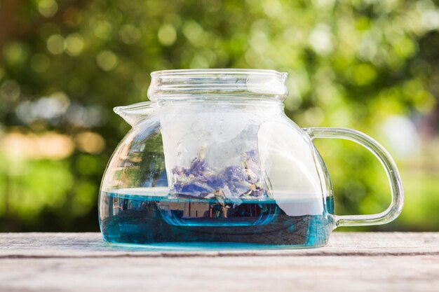 La teiera piena di tè blu e fiore di pisello di farfalla essiccato si trova su un tavolo di legno all'aperto