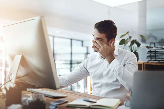 La tensione di una lunga giornata lo ha messo fuori combattimento Inquadratura di un giovane uomo d'affari che sembra stressato e stanco mentre lavora in un ufficio