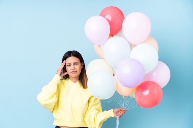 La tenuta della donna balloons in una festa sopra la parete blu isolata infelice e frustrata con qualcosa. Espressione facciale negativa