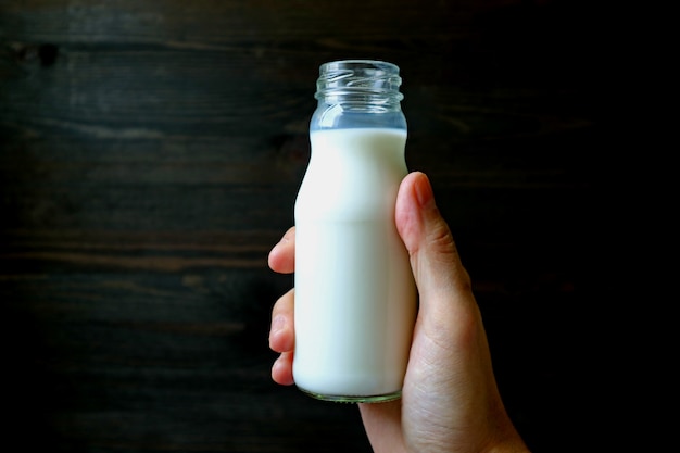 La tenuta della mano dell'uomo ha aperto la bottiglia di latte con la parete di colore scuro nel fondo