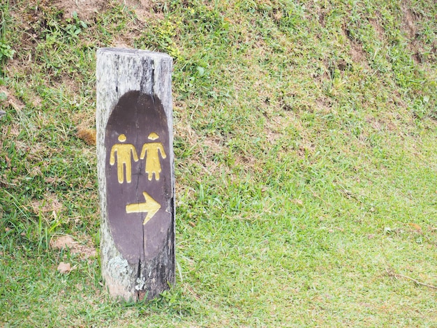 La toilette pubblica all&#39;aperto firma su legno sopra il campo di erba nel parco nazionale.