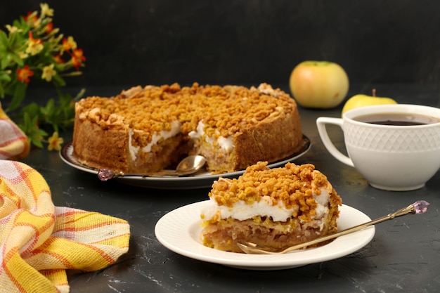 La torta con mele, meringhe e tazza di tè si trova su un piatto su una superficie scura