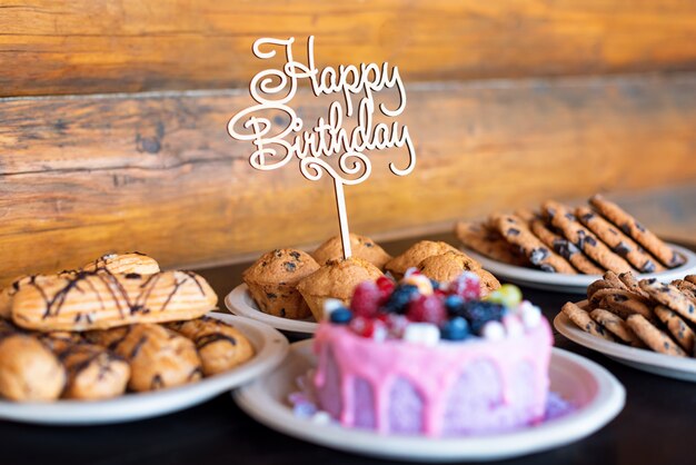 La torta e i muffin di compleanno con il saluto di legno firmano sulla parete rustica. Canto in legno con lettere Buon compleanno e dolci natalizi.