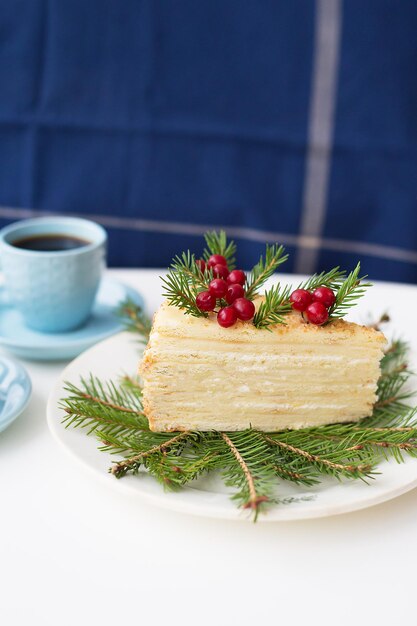 La torta ha decorato i rami e le bacche dell'albero di Natale su uno sfondo dell'albero di Natale e due tazze di caffè.