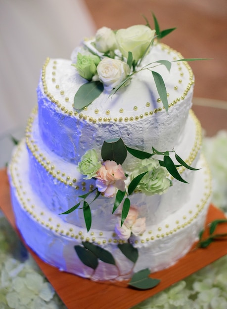 La torta nunziale bianca decorata con le rose bianche e le foglie verdi si leva in piedi sul piatto di legno