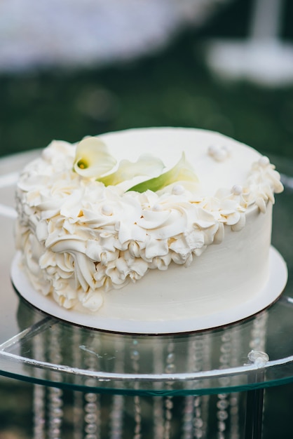 La torta nuziale bianca a un livello decorata con crema a forma di fiori si trova su un tavolo di vetro in natura