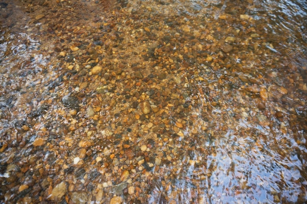 La trama del fondo. Le pietre visibili sotto l&#39;acqua limpida. Ondulazioni dell&#39;acqua del fiume, i raggi del sole sulle rocce.