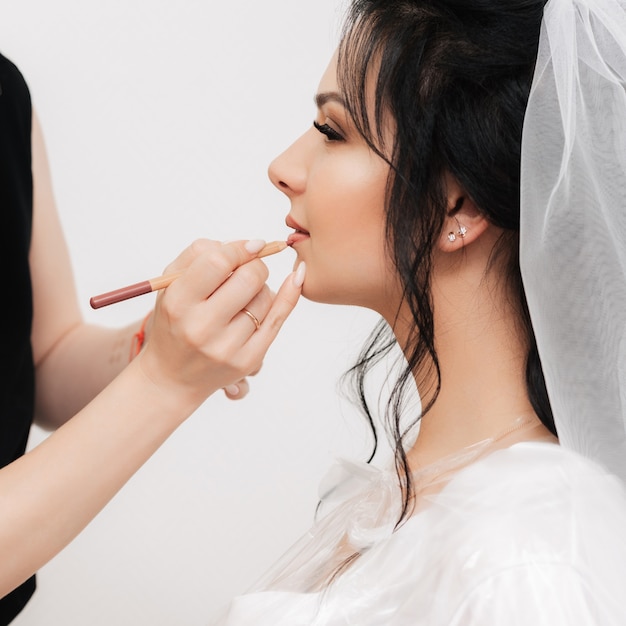 La truccatrice dipinge le labbra della donna della sposa con una matita in un salone di bellezza professionale