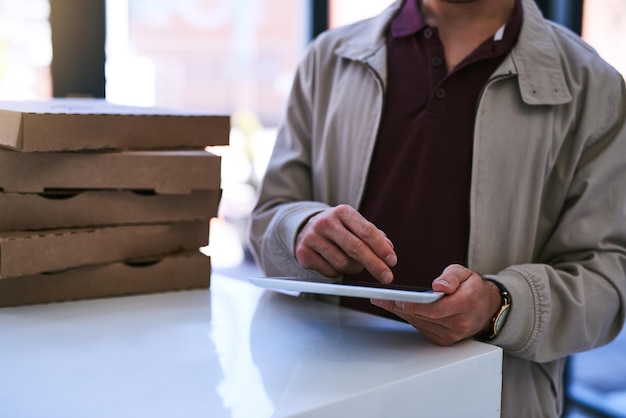 La tua consegna di pizza bollente è qui Foto ritagliata di un uomo che usa una tavoletta digitale mentre consegna una pizza