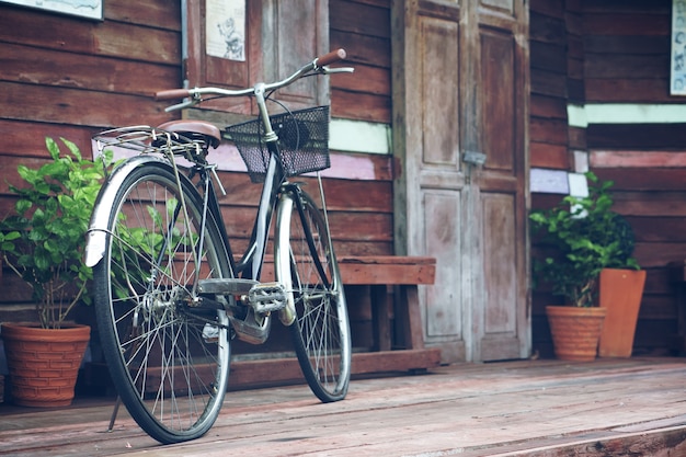 la vecchia bicicletta nera e marrone dell&#39;annata alla parte anteriore di retro terrazzo domestico di legno