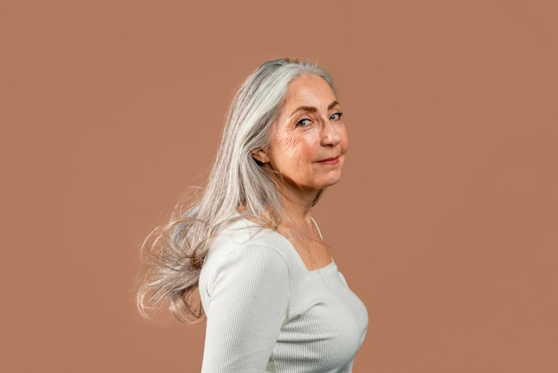 La vecchia femmina caucasica allegra con i capelli grigi di trucco naturale esamina la macchina fotografica gode della bellezza e della libertà