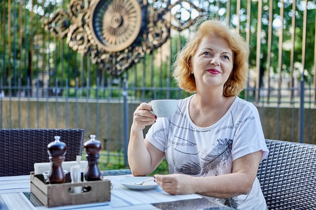 La vecchia femmina sorridente beve il caffè mentre si siede nel patio