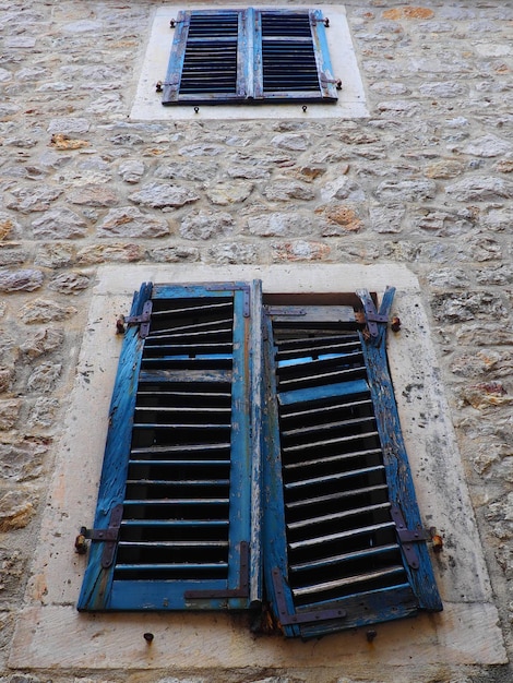 La vecchia finestra con persiane chiuse blu su una vecchia casa Texture vintage Herceg Novi Montenegro vecchia casa di pietra Architettura della regione adriatica Fissaggio di finestre e persiane al muro