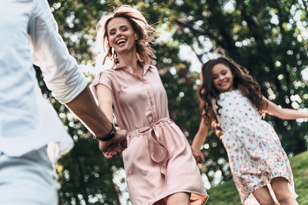 La vera gioia di essere solo in giro. Felice giovane famiglia di tre persone che si tengono per mano e sorridono mentre corrono nel parco