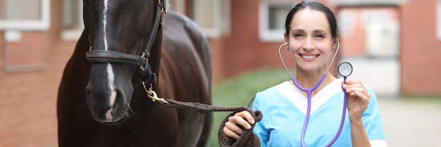 La veterinaria tiene in mano uno stetoscopio e si trova accanto al cavallo fornendo cure mediche a