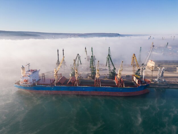 La vista aerea della grande nave portarinfuse viene caricata con chicchi di grano nel porto nella nebbia