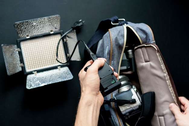 La vista dall'alto delle mani mette gli accessori della fotocamera nella borsa su una superficie scura