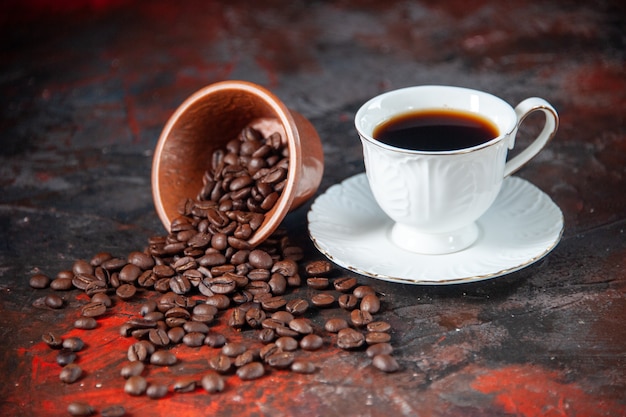 La vista dall'alto di un delizioso caffè in una tazza bianca e dei fagioli tostati è caduto da una ciotola di legno inclinata su uno sfondo di colore misto