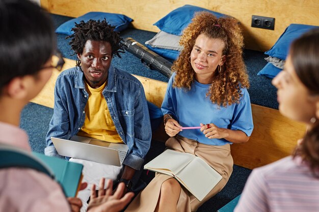 La vista dall'alto di un gruppo eterogeneo di studenti che studiano insieme in biblioteca si concentra sulla giovane donna sorridente