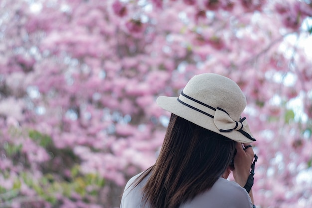 la vista di una donna itinerante con il cappello piacevole sta prendendo le immagini sulla priorità bassa dentellare del fiore.