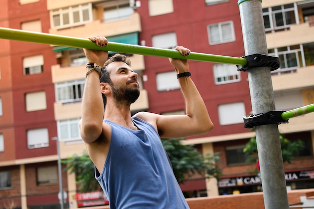 La vista frontale di un uomo caucasico che fa la barra spinge verso l'alto con l'espressione del dolore