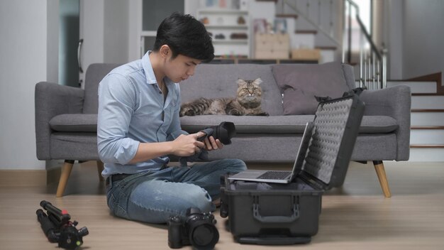 La vista laterale del giovane fotografo mette gli accessori della fotocamera nella borsa mentre è seduto sul pavimento di legno a casa.