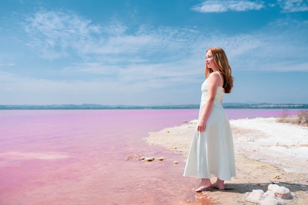 La vista laterale della donna sveglia dell'adolescente che indossa l'estate copre sul lago rosa