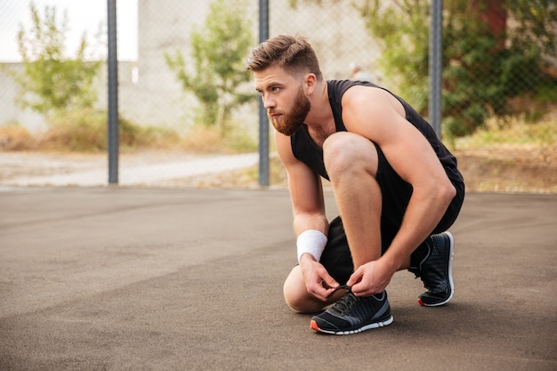 La vista laterale di un atleta dell'uomo di sport lega i suoi lacci delle scarpe all'aperto