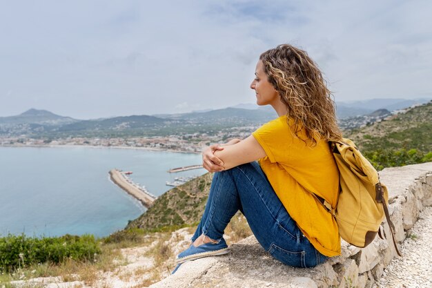 La vista orizzontale della donna si siede sulla cima di una montagna. Stile di vita estivo e avventura con zaino.