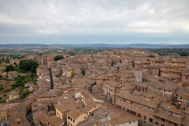 La vista panoramica della città di Siena con edifici storici e campi verdi lontani da Torre del Mangia è una torre in città. Giornata di sole estivo e cielo blu drammatico