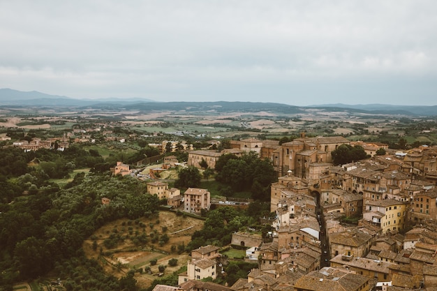 La vista panoramica della città di Siena con edifici storici e campi verdi lontani dalla Torre del Mangia è una torre in città. Giornata di sole estivo e cielo blu drammatico