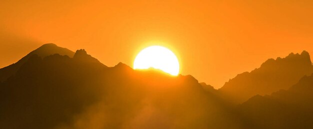 La vista panoramica delle montagne a silhouette contro il cielo arancione