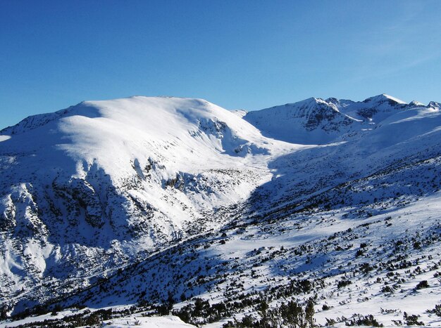 La vista panoramica delle montagne innevate contro un cielo azzurro limpido