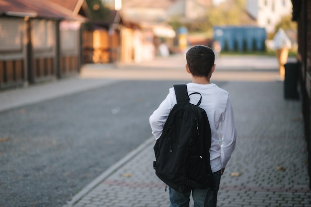 La vista posteriore del ragazzo in camicia bianca con zaino nero va a casa dopo la lezione
