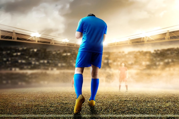 La vista posteriore dell'uomo del giocatore di calcio asiatico in una maglia blu celebra la vittoria