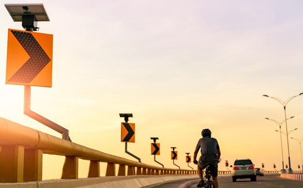 La vista posteriore dell'uomo indossa il casco in sella alla bicicletta sulla strada curva dietro le auto Guida sicura su strada