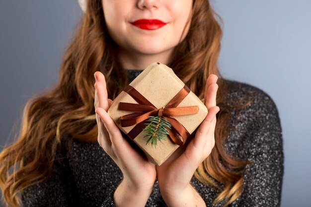 La vista ravvicinata delle mani e delle labbra ti sta regalando una bella confezione regalo, una donna che fa regali e saluta il concetto di stagione su sfondo grigio isolato