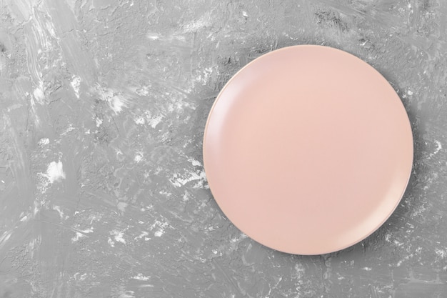 La vista superiore del piatto rosa vuoto rotondo opaco sullo spazio scuro del fondo del cemento per voi progetta