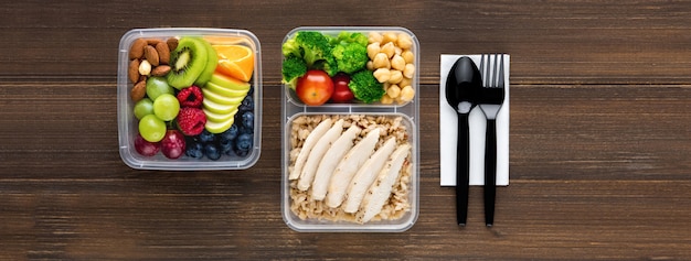 La vista superiore dell'alimento ricco nutriente sano messa dentro porta via le scatole con il cucchiaio e la forchetta sul fondo di legno dell'insegna della tavola
