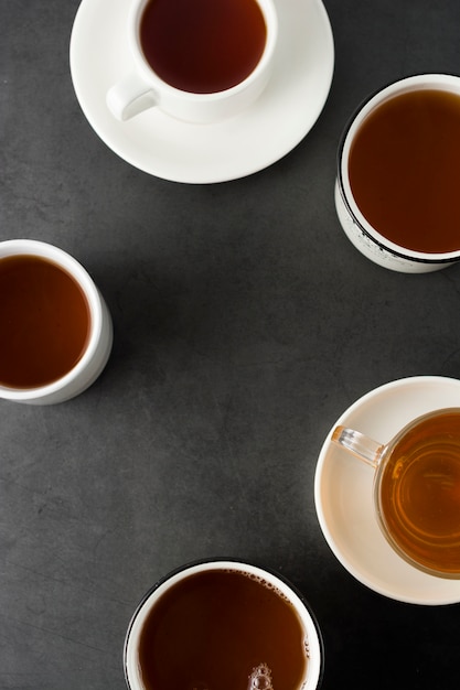 La vista superiore di molte tazze, tazze con tè caldo beve su oscurità, copyspace. Ora del tè o freno del tè. Bevanda autunnale. Immagine tonica con tazze da tè.