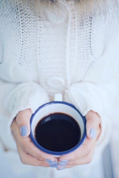 La vista superiore e la fine sulle mani della donna che tengono la tazza di caffè o il tè calda nel freddo