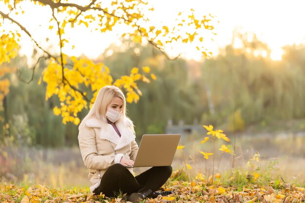 La vita ai tempi del covid-19. Giovane donna che indossa una maschera protettiva che digita sul computer portatile in un parco pubblico. Elegante donna che utilizza il computer mentre si lavora all'aperto. Didattica a distanza e lavoro a distanza durante la pandemia