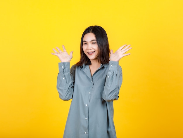 La vivace donna asiatica in camicia a maniche lunghe gode di un ritratto isolato della moda femminile alzando la mano, sorridendo, gesticolando mentre trasporta l'offerta di opportunità sorprese sopra e felice su una promozione attraente