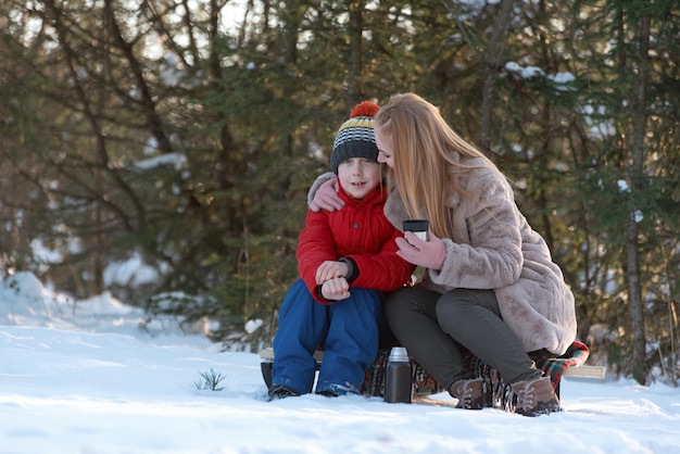 La zia madre o la sorella maggiore abbracciano un ragazzo adolescente in inverno fuori Picnic nella foresta coperta di neve Inverno