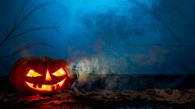 La zucca di Halloween su uno sfondo di legno in un'atmosfera inquietante con candele e fumo