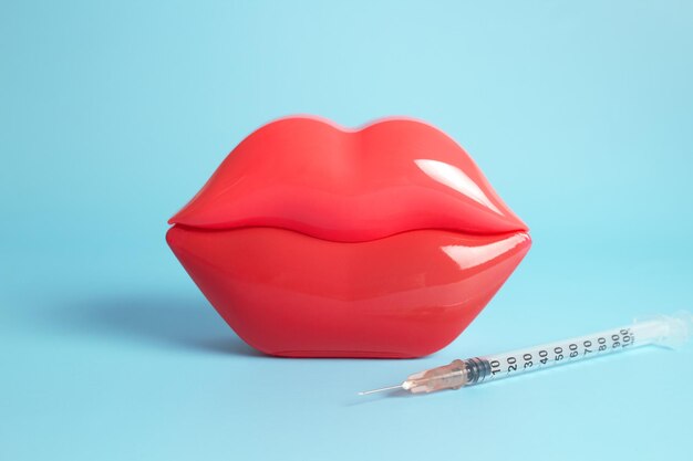 Labbra femminili in plastica rossa brillante e una siringa per iniezione di riempitivo e acido ialuronico