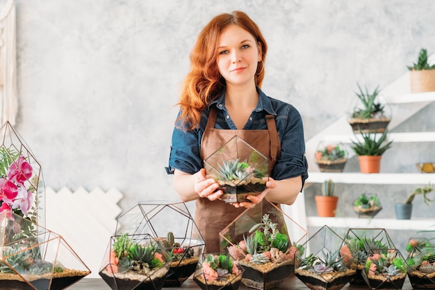 Laboratorio di decorazioni floreali per interni. Donna che tiene vaso di vetro con piante grasse che crescono in vaso di vetro.