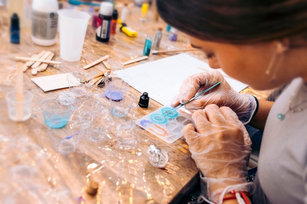 Laboratorio di gioielleria con resina epossidica Primo piano delle mani guantate di una donna con pinze per gioielli