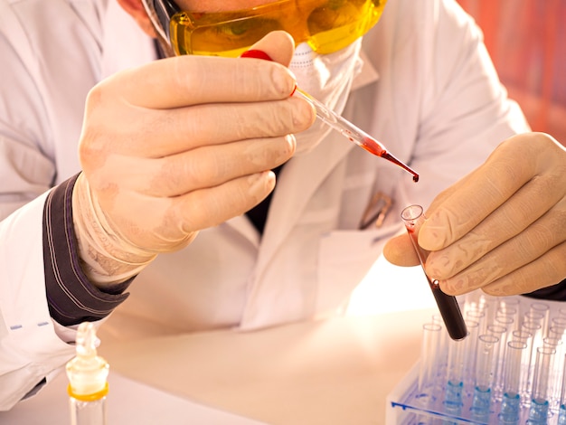 Laboratorio moderno. Il ricercatore fa cadere un campione di sangue in una provetta. Concentrati su una goccia di sangue.