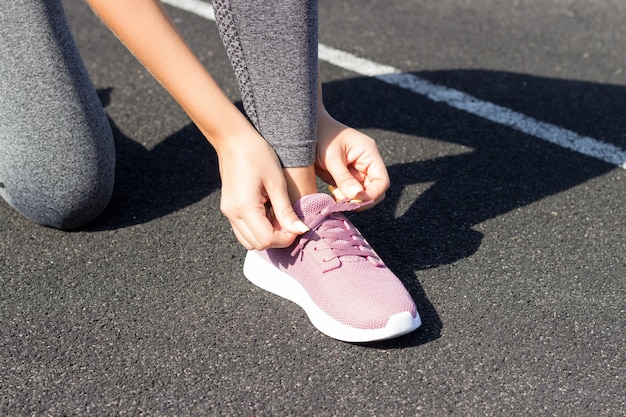 Lacerazioni della ragazza sulle sue scarpe da ginnastica rosa per la corsa. primo piano senza volto. Concetto di aria aperta, luce solare, stadio, sport e fitness